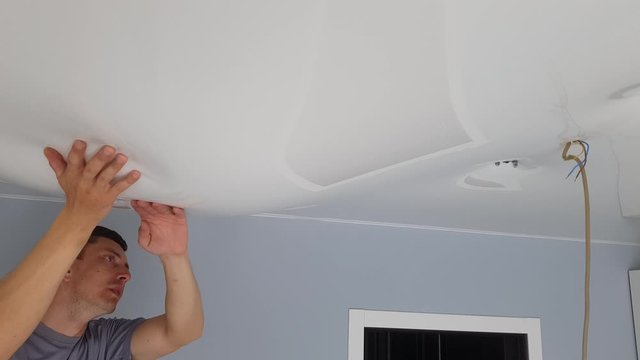 Men is drain water from a stretch ceiling filled with water through a tube. Flood, water leakage from the ceiling in the apartment.