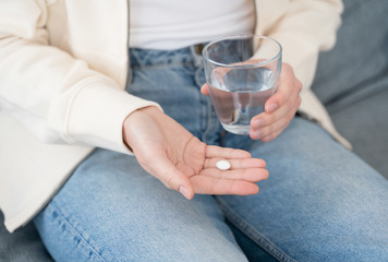 Closeup of woman open palm with medical capsule and another hand with glass of water, taking care about health, girl willing to cope with pain