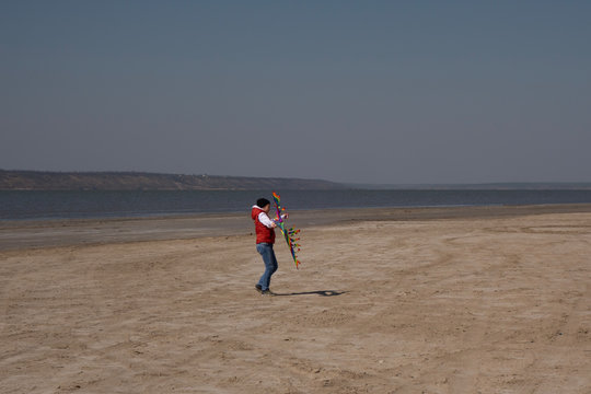 A 10 Year Old Boy In A White Sweatshirt And Orange Vest Launches A Kite On A Deserted Beach In Solitude.