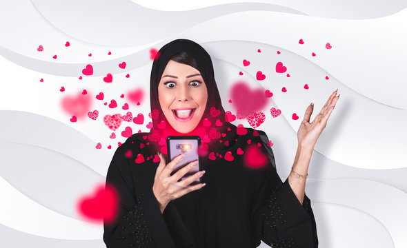 Beautiful happy Arab woman received love text message on mobile phone with pink hearts flying away from screen standing on gray background. Positive human emotions face expressions - Powered by Adobe