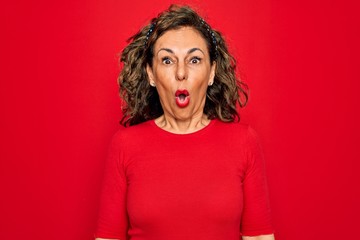 Middle age senior brunette woman wearing casual t-shirt standing over red background afraid and shocked with surprise expression, fear and excited face.