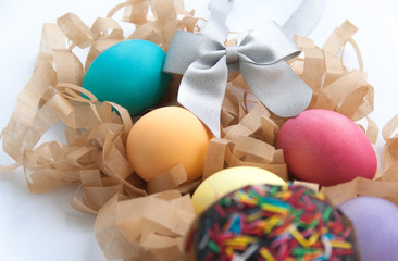 Easter cake, colourful eggs on hay and silver bow on white table. Close up