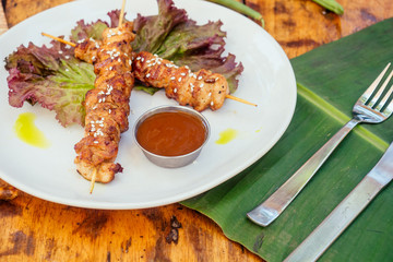 asian tropical style kebab on the plate with banana and lettuce leaves and sesame seeds on wooden table