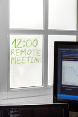 Space with devices at home to teleworking, detail of a reminder written on the window "Remote Meeting". Concept of working from home, telecommuting.