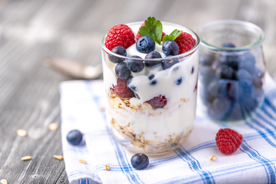 White yogurt in glass jar with raspberries and blueberries on napkin.