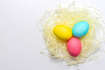 Colored Easter eggs in nest isolated on white background. Happy holiday card, close-up, top view, copy space