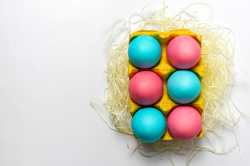 Blue and pink Easter eggs in yellow paper egg tray isolated on white background. Top view, close-up, copy space