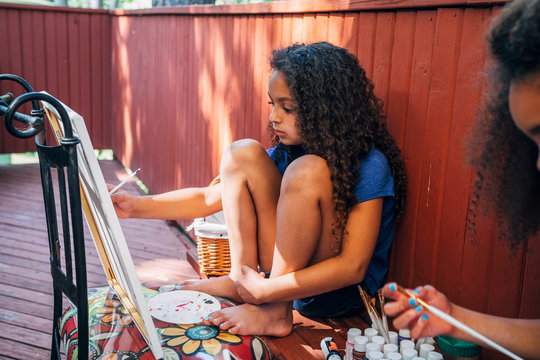 Girl painting on canvas outside on deck of home