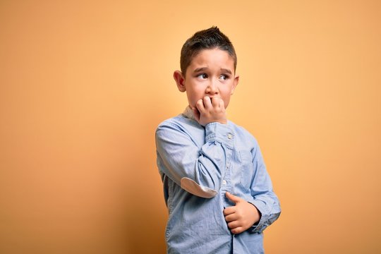 Young Little Boy Kid Wearing Elegant Shirt Standing Over Yellow Isolated Background Looking Stressed And Nervous With Hands On Mouth Biting Nails. Anxiety Problem.