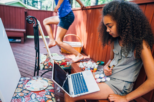 Girls Sitting On Deck Learning To Paint From Online Video On Laptop