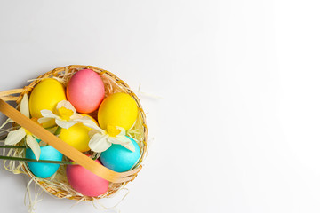 Colored Easter eggs and narcissus flowers  in a basket at the corner isolated on white background. Easter idea design, postcard, wallpaper, copy space, top view