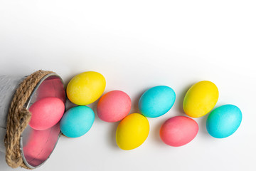 Fototapeta na wymiar Colored Easter eggs near small white bucket isolated on white background. Easter wallpaper and postcard, top view, close-up, copy space