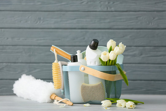 Set of cleaning supplies and spring flowers on grey wooden background