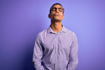 Obraz premium Handsome african american man wearing striped shirt and glasses over purple background looking at the camera blowing a kiss on air being lovely and sexy. Love expression.