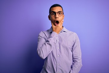 Handsome african american man wearing striped shirt and glasses over purple background Looking fascinated with disbelief, surprise and amazed expression with hands on chin