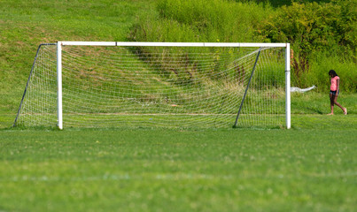 a lonely African-American girl walks by an empty soccer goal and field on a sunny summer afternoon