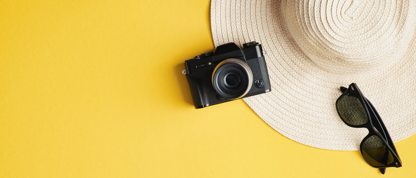 Flat lay summer female fashion straw hat, sunglasses, vintage camera on yellow background. Top view stylish traveler accessories. Summer holiday vacation, travel, tourism concept