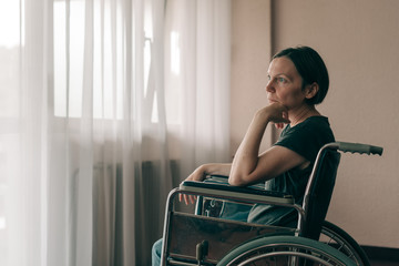 Obraz na płótnie Canvas Depressed sad woman in worn wheelchair looking out the window