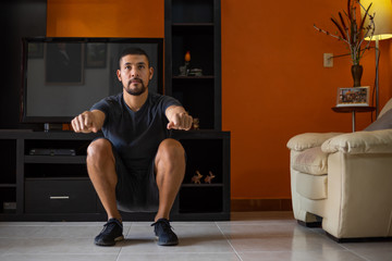 Naklejka premium man doing squats at home due to coronavirus pandemic in Mexico in living room with black sports 