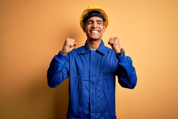 Young handsome african american worker man wearing blue uniform and security helmet excited for success with arms raised and eyes closed celebrating victory smiling. Winner concept.