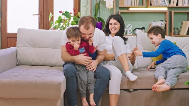 Couple chatting on the sofa their two kids running to them and sitting on the sofa all together playing and smiling large speeding a good time. Shot on ARRI Alexa Mini