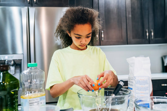 Girl breaking egg into bowl to bake recipe