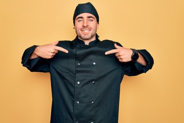 Young handsome cooker man with blue eyes wearing uniform and hat over yellow background looking confident with smile on face, pointing oneself with fingers proud and happy.