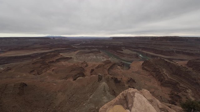 An ultra-wide timelapse looking down towards a gooseneck in the Colorado River and towards Canyonlands National Park as seen from Dead Horse Point. A thick layer of cloud flows overhead.
