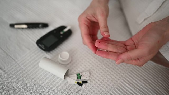  Diabetes checking blood sugar level. Woman using lancelet and digital glucometer at home. Medicine, diet diabetes, health care concept - female hands with glucometer checking body glucose level