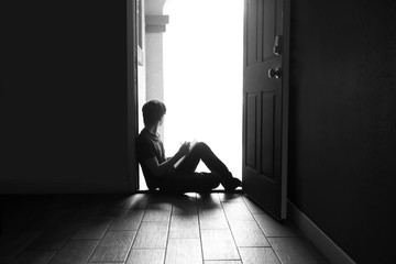 young teen boy sits in doorway looking out while doing schoolwork at home