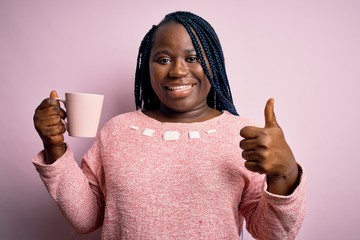 African american plus size woman with braids drinking mug of coffee over pink background happy with...