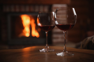 Glasses of red wine near fireplace indoors. Space for text