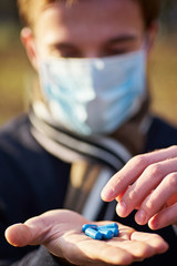 guy in a medical mask holds out his hands with pills to the camera. Concept photo on the Covid 19 pandemic