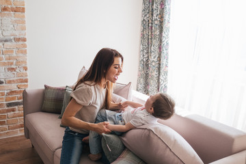 Young beautiful mother plays with her son in a sunny room. Silit with a child on the floor on the...
