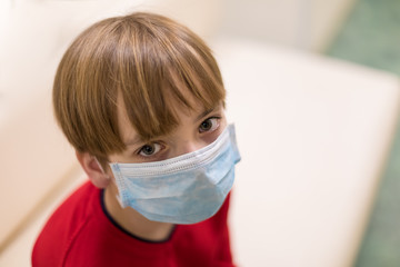 Caucasian boy wearing a medical mask on his face. Large portrait. The baby looks into the camera. concept of visiting public places as a pre-official measure against the COVID-19 coronavirus