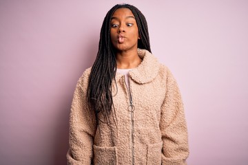 Young african american woman wearing fashion winter coat over pink isolated background making fish face with lips, crazy and comical gesture. Funny expression.