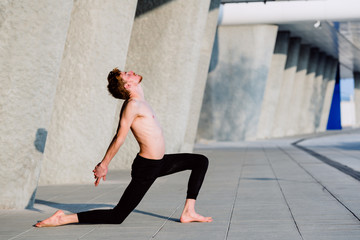 Fototapeta na wymiar Young man performing joint movement exercise inspired by yoga, outdoors.