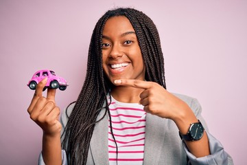 Young african american girl holding small car as transport insurance over isolated pink background very happy pointing with hand and finger