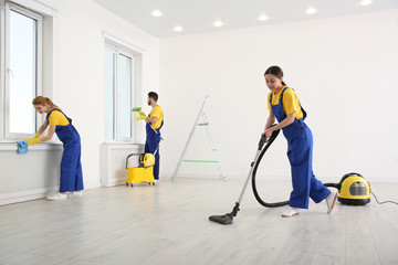 Team of professional janitors in uniforms cleaning room