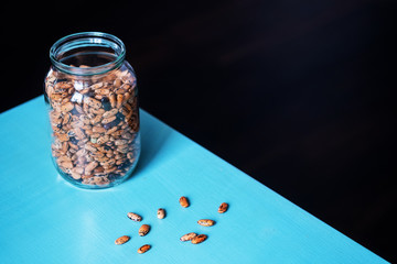 Pinto beans in a glass jar with grains on the table on a black background with empty space on the left. Minimalist style shot