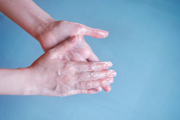 Color and bright shot of young woman lathers her hands on a blue background from bacteria and the virus. An example of how to wash and soap your hands