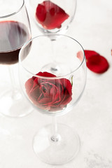 Glasses with rose and wine on light background