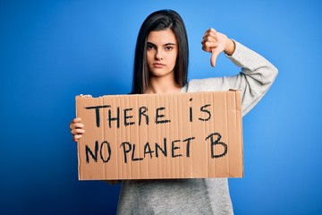 Young beautiful brunette activist woman holding banner protesting to care the planet with angry...