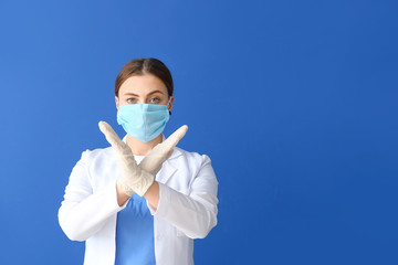 Doctor in protective mask showing stop gesture on color background. Concept of epidemic