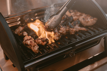 Grill season outdoor in park or balcony. Spring summer grilling. Balcony gas grill. Barbeque fourth of July weekend. Chicken wings on grill. Flame and smoke over grill. BBQ quarantine on balcony.