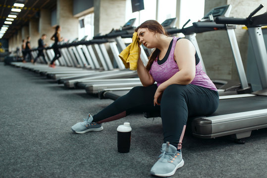 Tired overweight woman sitting on treadmill in gym