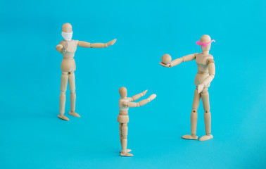 Concept - ban on ball games with children during quarantine. Group of wooden little men mannequins. A man in a protective medical mask prohibits others from playing actively. Social distance.