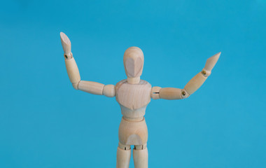 Wooden man manikin raised hands up, standing on a blue background.