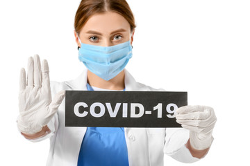 Doctor in protective mask holding paper sheet with text COVID-19 on white background. Concept of epidemic