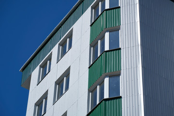 facade of a new multistory building with white and green metal siding, many Windows
